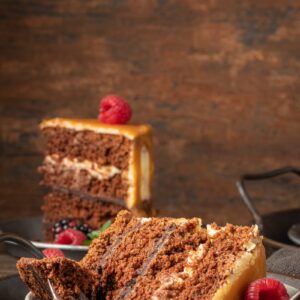 Delicious semi-naked chocolate cake with caramel topping and decorated with blackberries and raspberries. Dark background